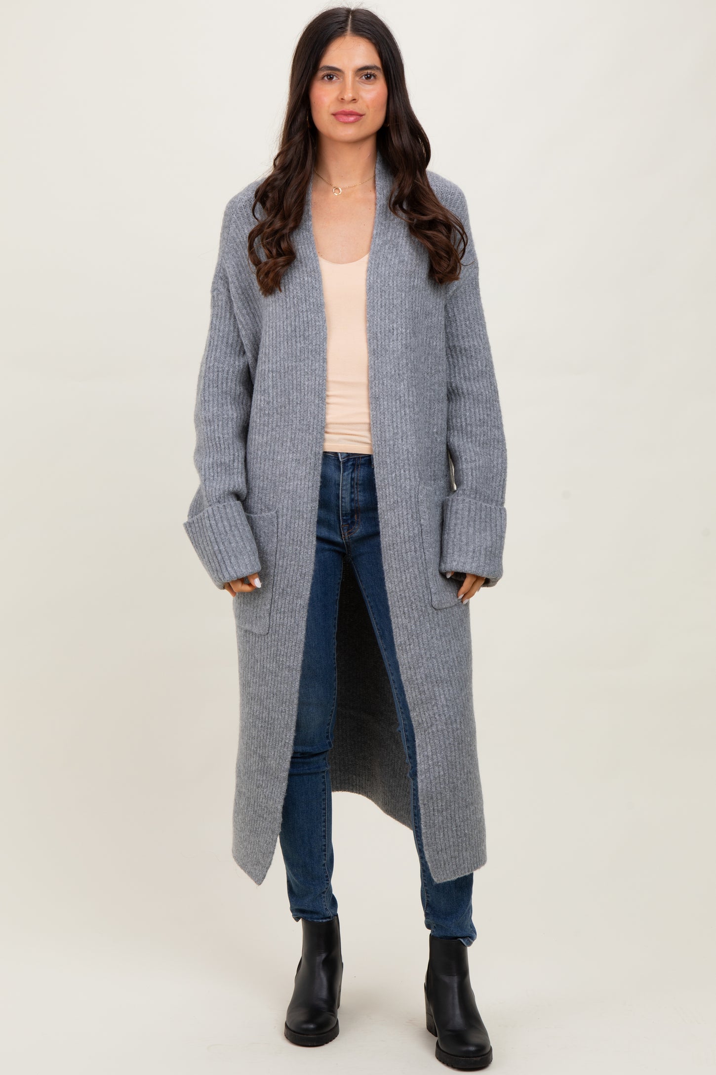 woman wearing a long gray ribbed cardigan over a light peach tank top and blue jeans