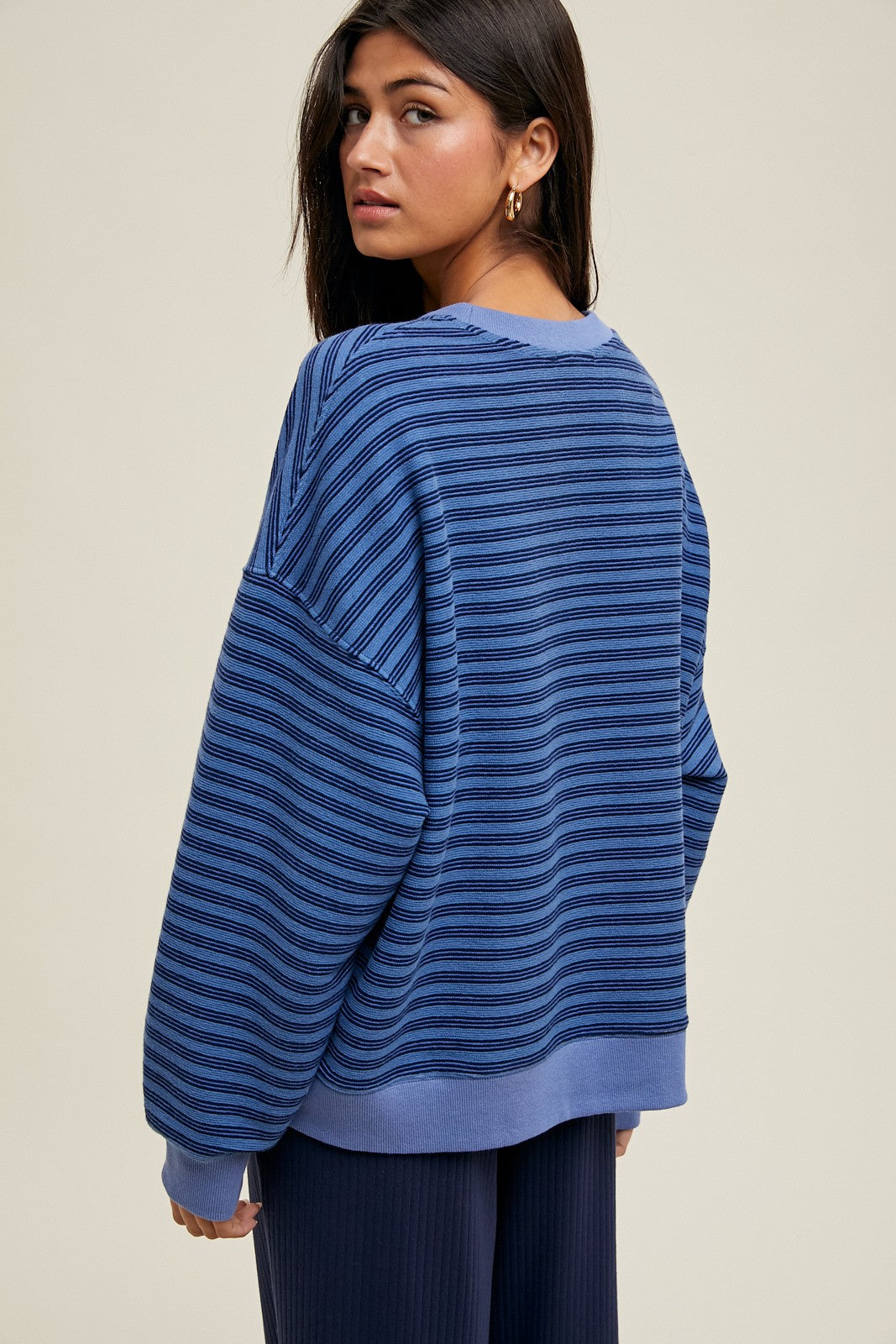 woman wearing a blue striped oversized sweater, showing the back and relaxed fit, paired with dark ribbed pants