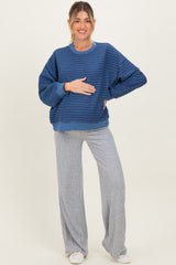 woman wearing a blue striped maternity sweatshirt and gray ribbed maternity pants, cradling her baby bump