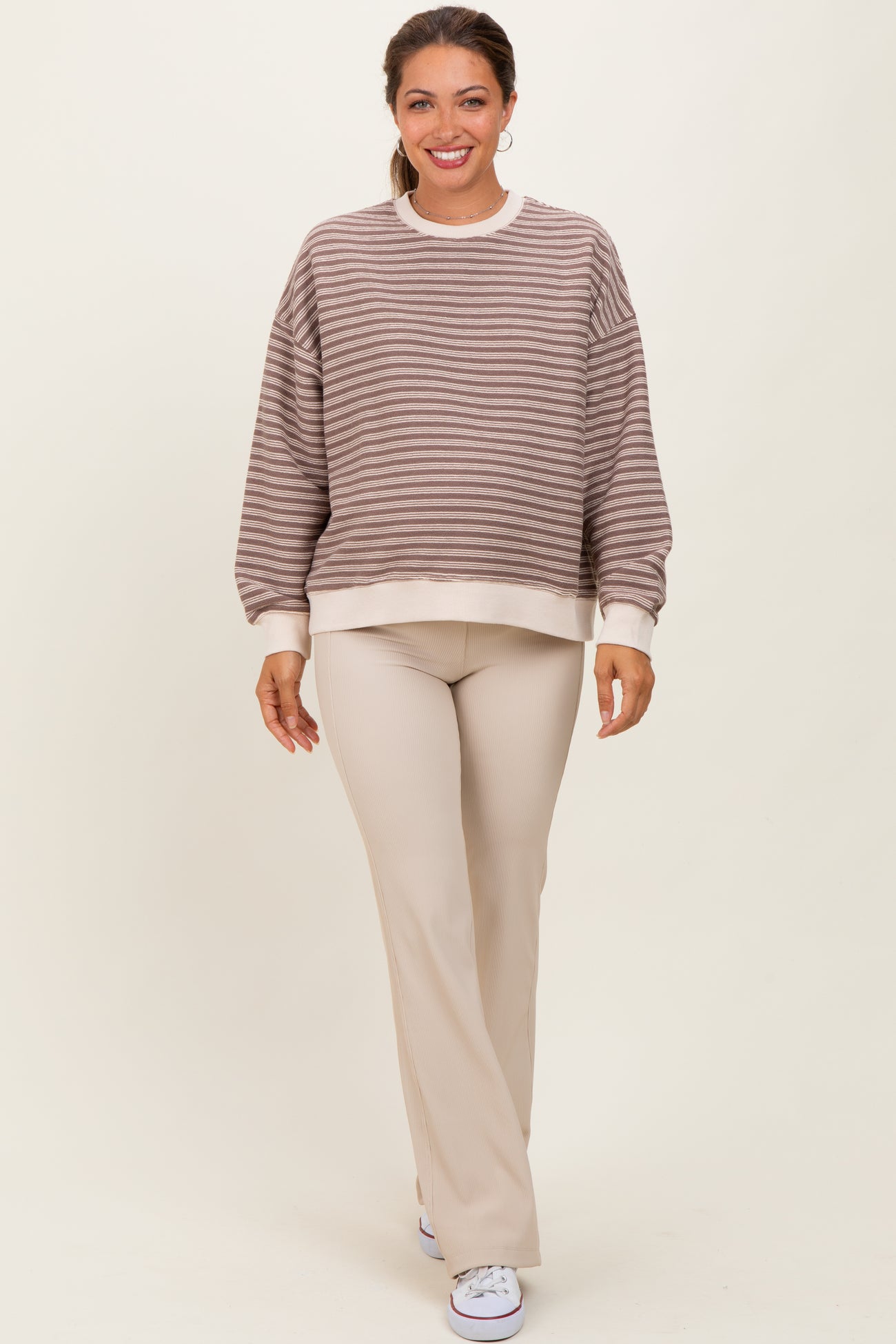woman wearing a beige and brown striped maternity sweatshirt paired with beige ribbed maternity pants