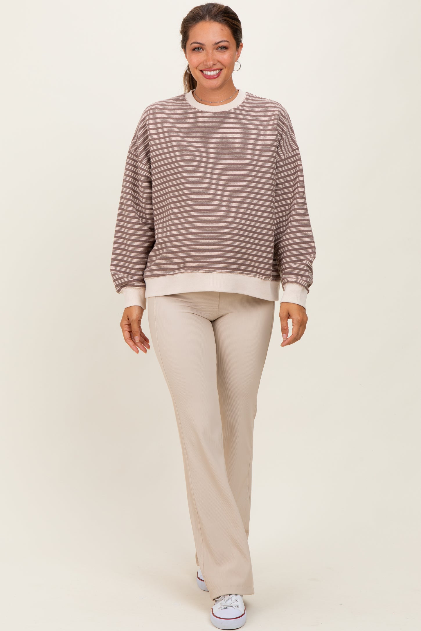 woman wearing a beige and brown striped maternity sweatshirt paired with beige ribbed maternity pants