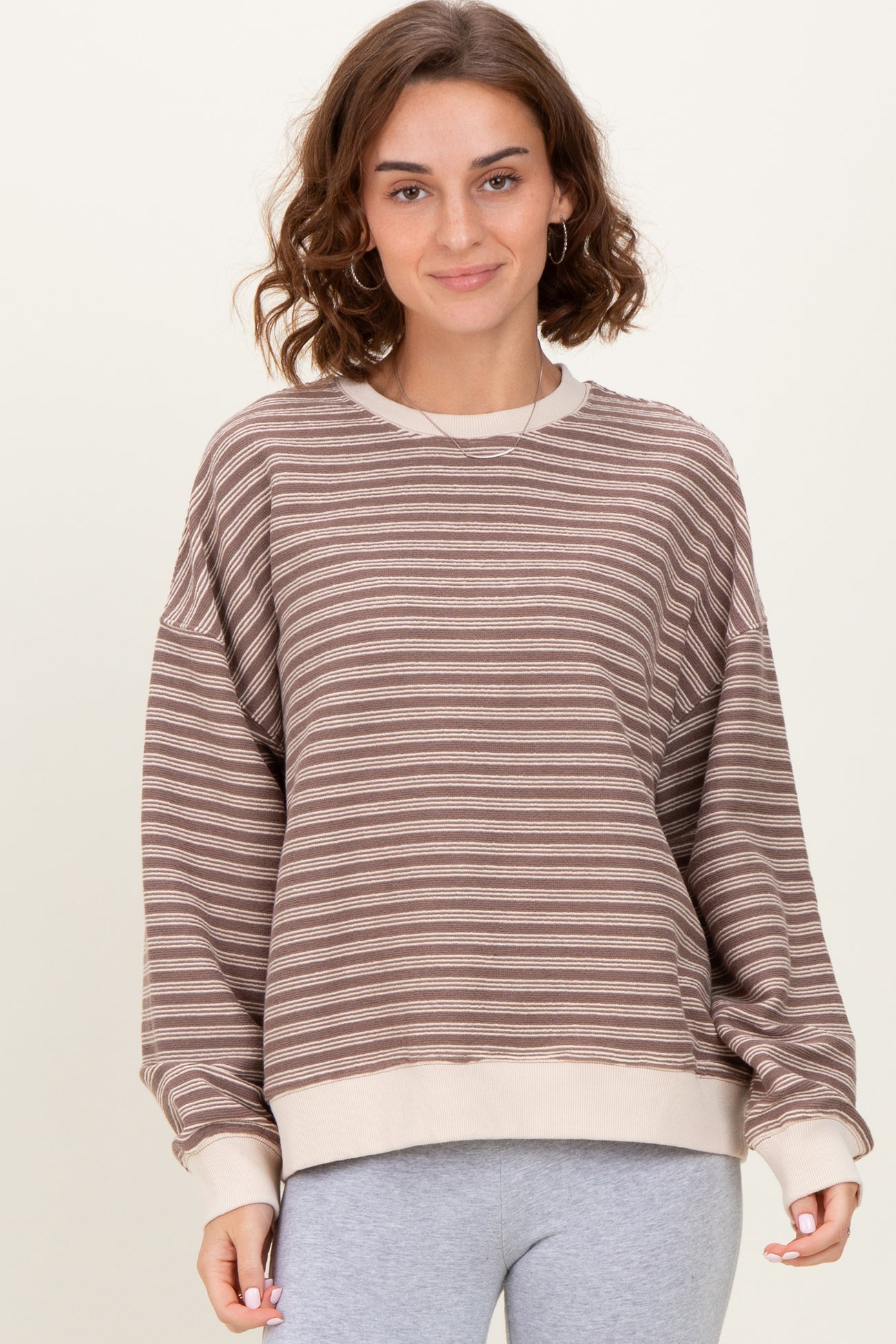 woman wearing a brown and cream striped oversized sweatshirt with a ribbed hem and relaxed fit