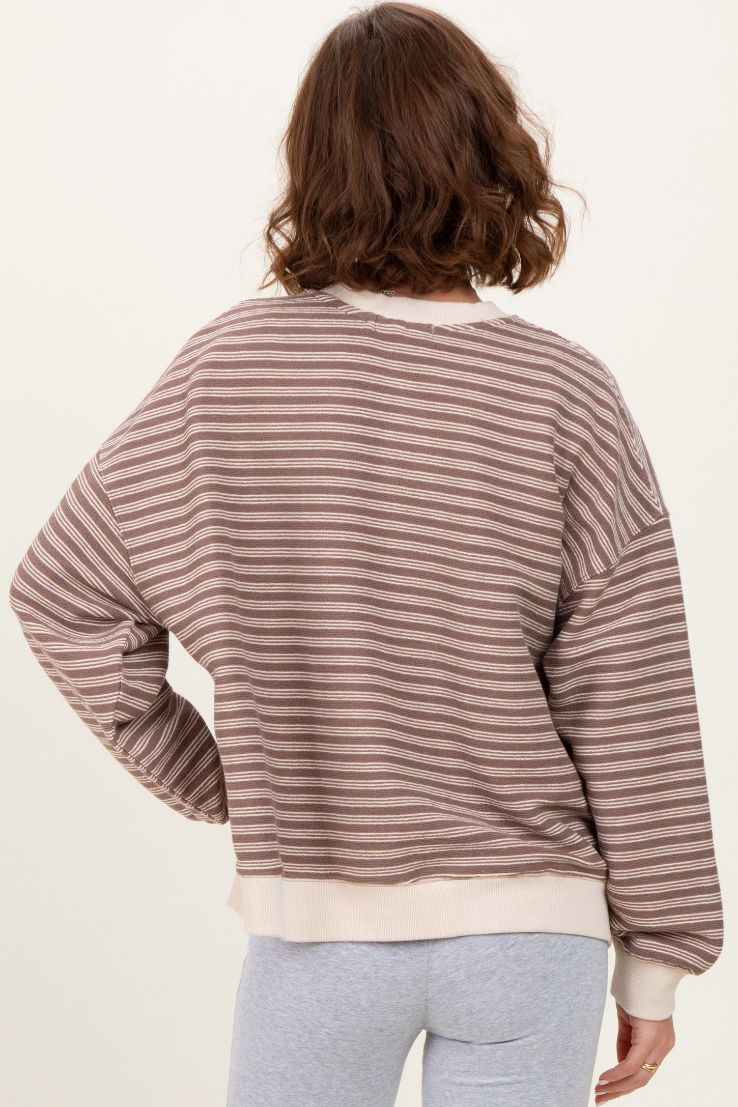 woman wearing a brown and cream striped oversized sweater, view of the back with relaxed fit and ribbed hem
