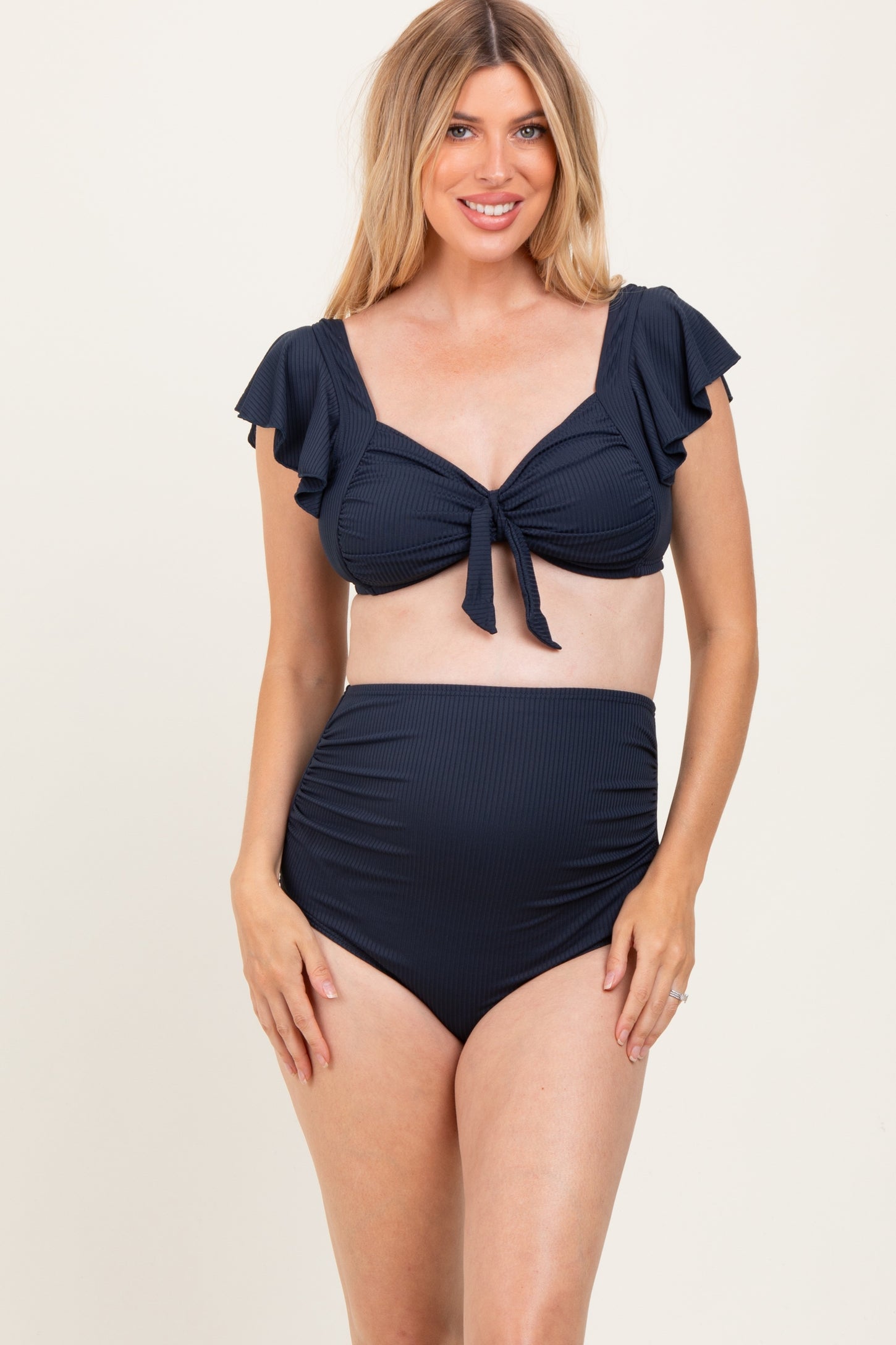 woman wearing a navy blue maternity bikini with ruffled sleeves and high-waisted bottoms, showing a baby bump