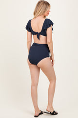 woman wearing a navy blue maternity bikini with ruffled sleeves and high-waisted bottoms, showcasing a side view
