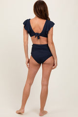 woman wearing a navy blue bikini with ruffled sleeves and a tied back, showing the back view and high-waisted bottoms