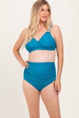 woman wearing a teal maternity bikini with a scalloped edge top and high-waisted bottoms