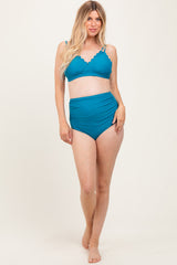 woman wearing a teal maternity bikini with scalloped detailing and high-waisted bottoms, showing her baby bump
