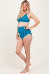 woman wearing a teal maternity bikini with scalloped details and a visible baby bump