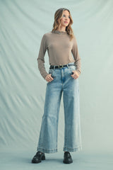woman wearing a beige and brown striped long sleeve top and wide leg light wash jeans, styled with a belt and black shoes