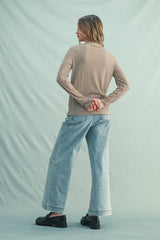 woman wearing a brown and beige striped long sleeve top and light blue wide-leg jeans, standing with hands behind her back