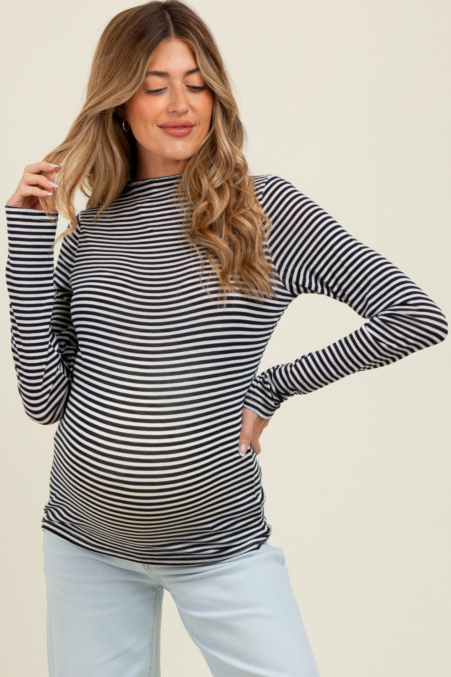 woman wearing a black and white striped maternity top, showing her baby bump, paired with light blue pants