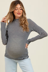 woman wearing a black and white striped maternity top, showing her baby bump, paired with light blue pants