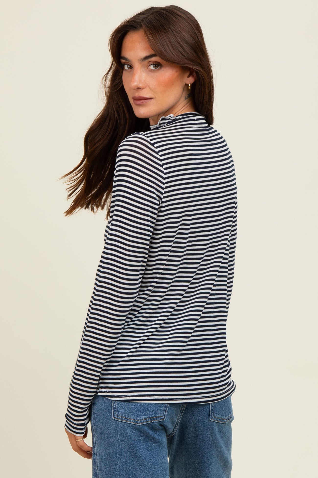 woman wearing a black and white striped long sleeve top with a high neck, seen from the back, paired with blue jeans