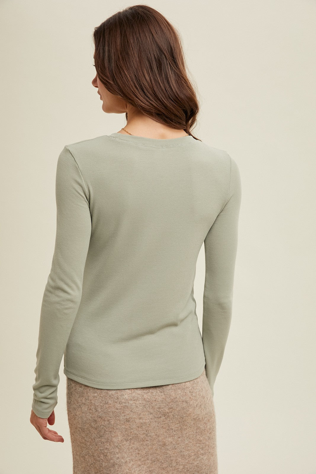 woman wearing a light green long sleeve ribbed top, viewed from the back, paired with a beige skirt