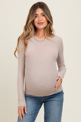 woman wearing a beige long sleeve maternity top and holding her baby bump