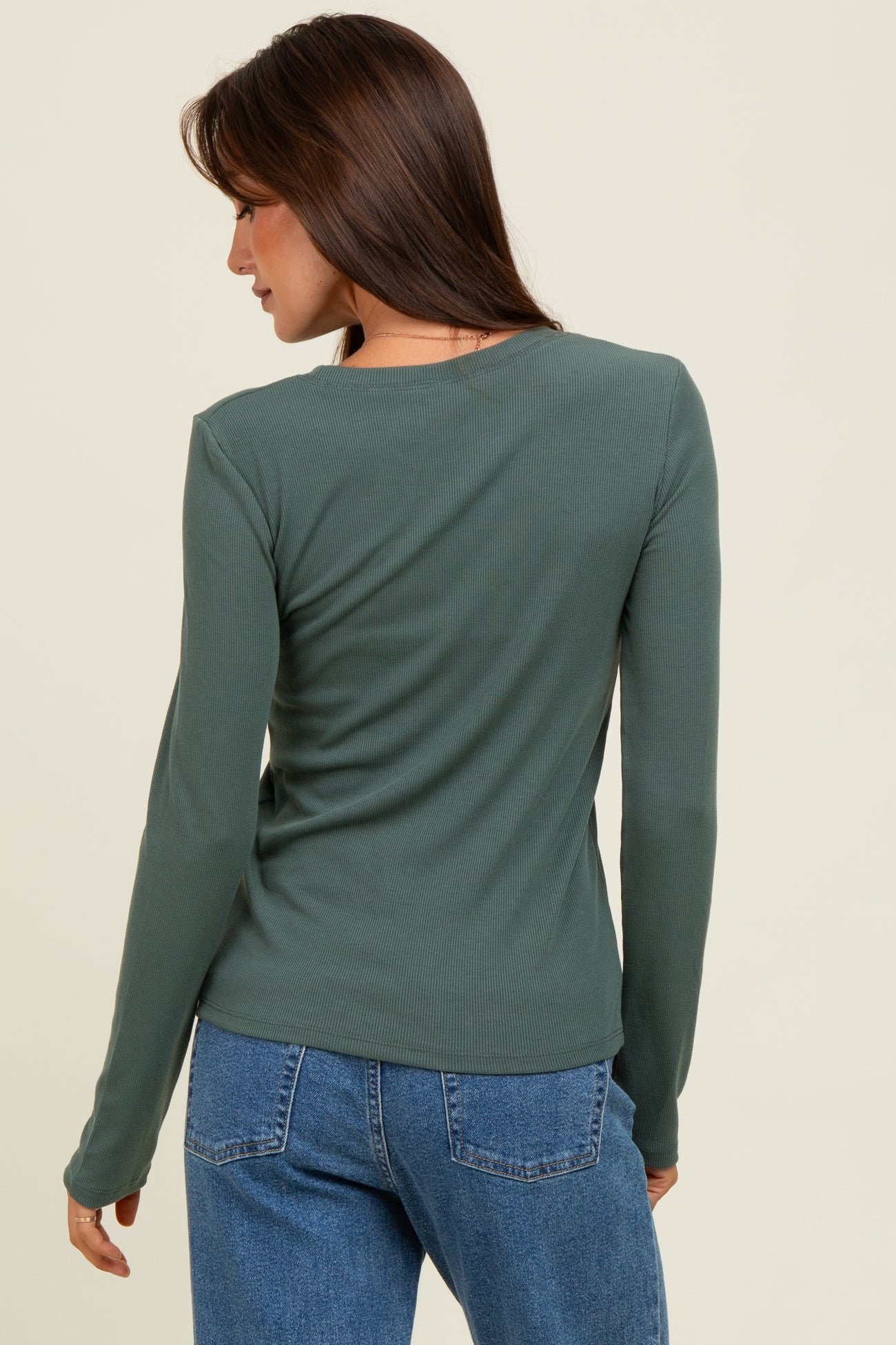 woman wearing a dark green long sleeve ribbed top, seen from the back with casual blue jeans