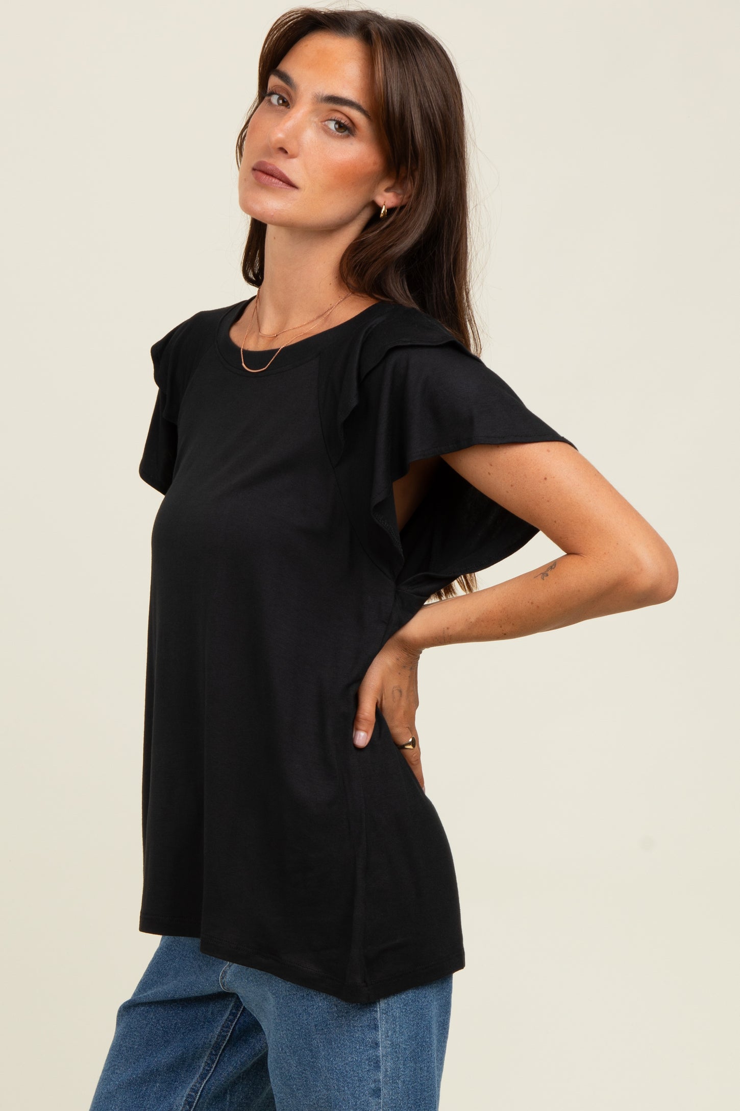 woman wearing a black short sleeve top with ruffle details, paired with blue jeans