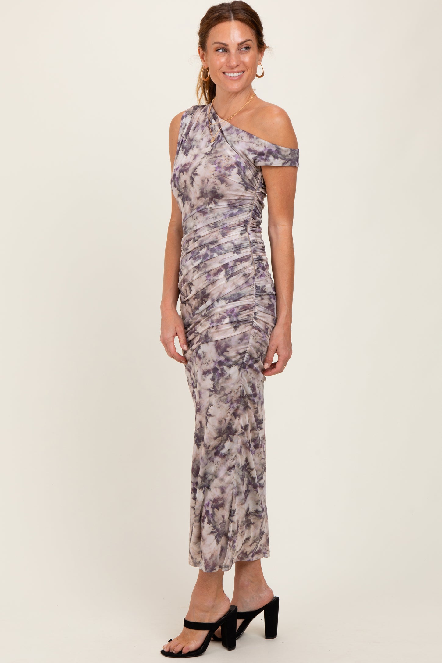 woman wearing a one-shoulder midi dress in a purple and gray tie-dye pattern, styled with black heeled sandals