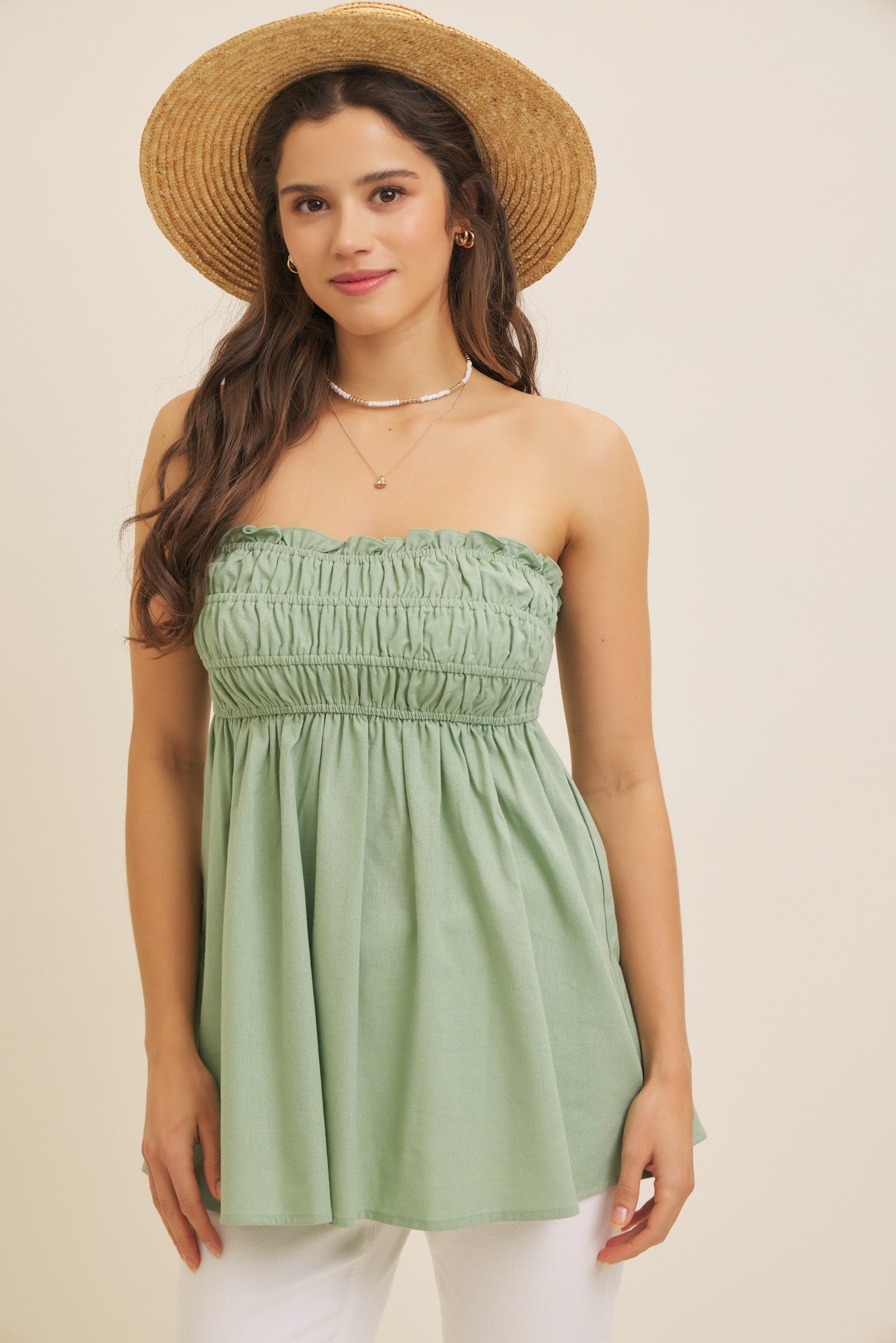 woman wearing a strapless green smocked blouse with a flowy silhouette and a straw hat