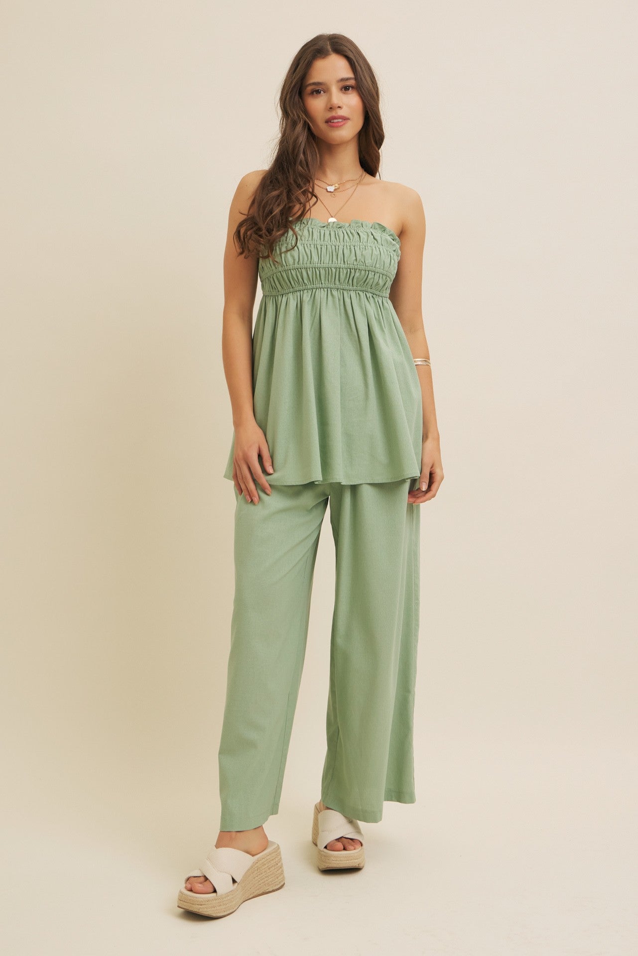 woman wearing a light green strapless smocked top and matching wide-leg pants with platform sandals