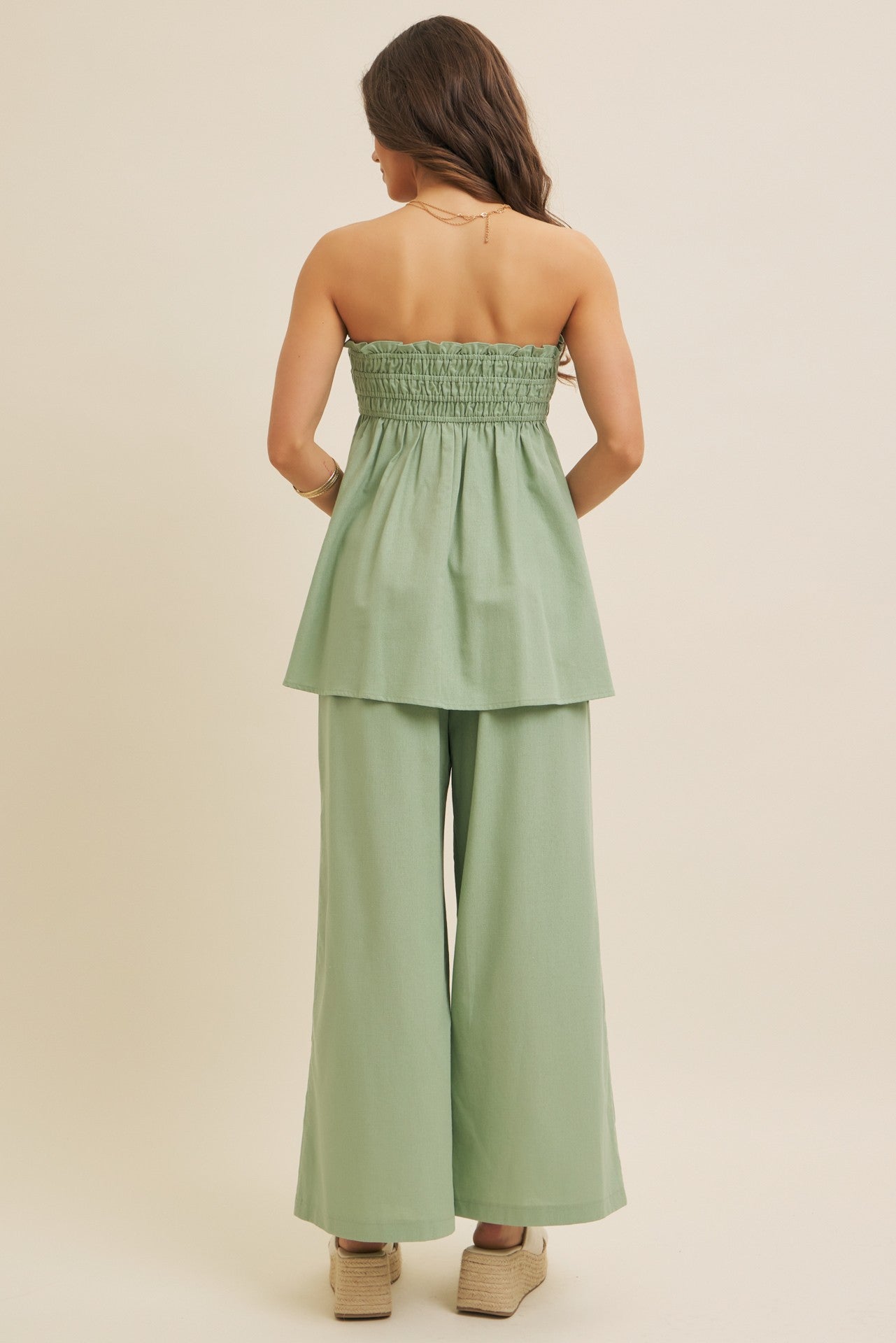 woman wearing a strapless sage green peplum top and wide-leg pants, styled with wedge shoes, seen from the back