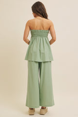 woman wearing a strapless sage green peplum top and wide-leg pants, styled with wedge shoes, seen from the back