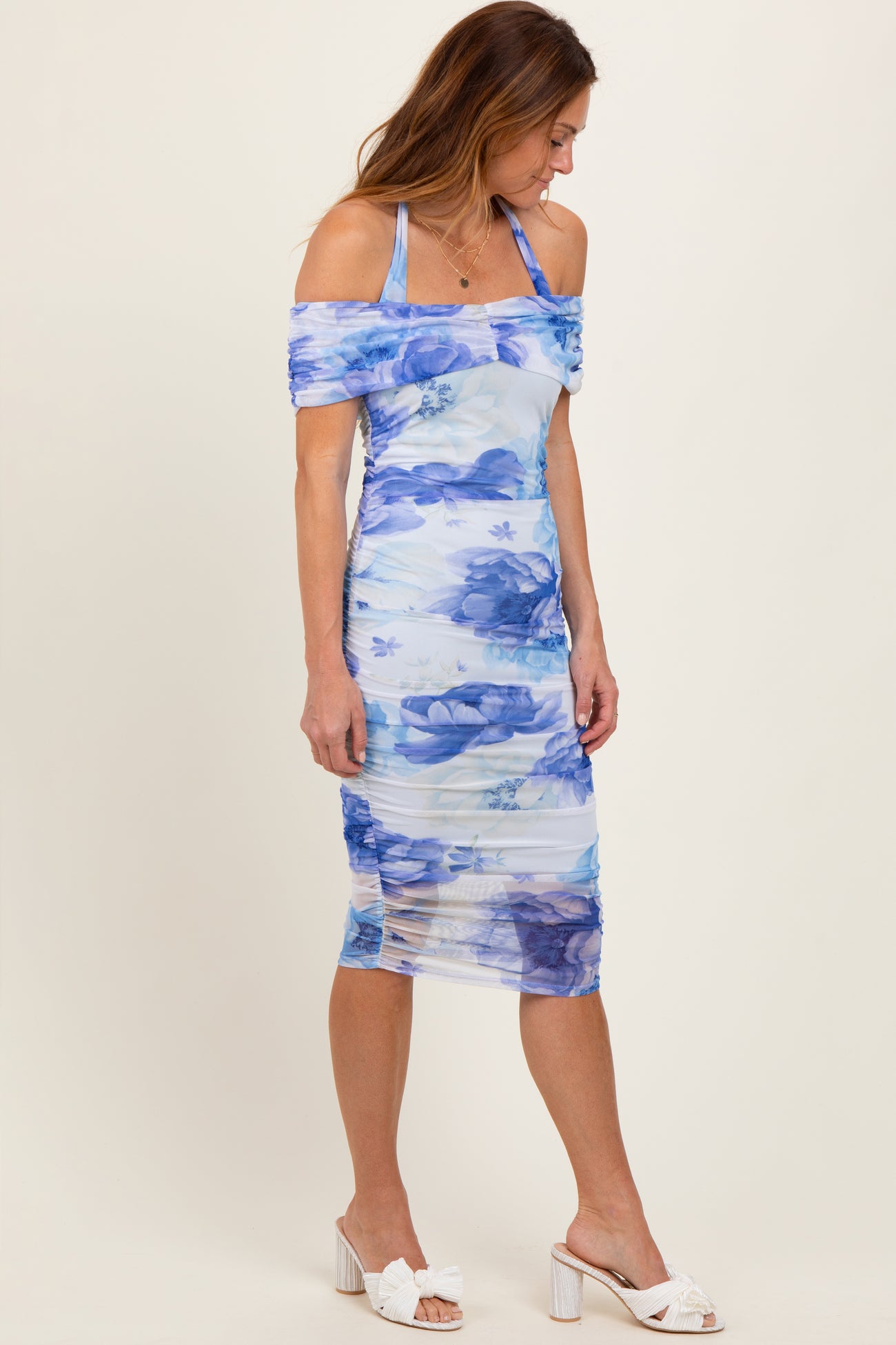woman wearing a blue floral off-the-shoulder midi dress with ruching and strappy details, paired with white heels