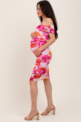 woman wearing a pink floral off-the-shoulder maternity dress and holding her baby bump