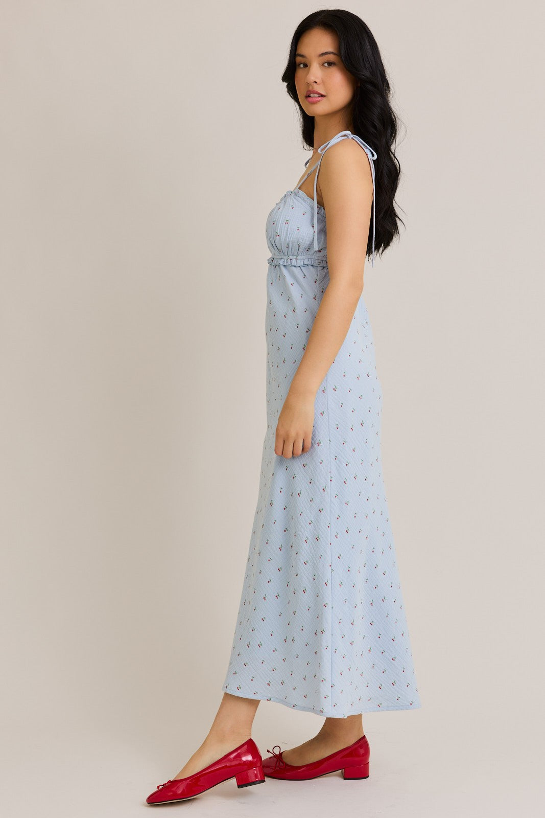 woman wearing a light blue floral maxi dress with adjustable straps and side slits, paired with red flat shoes