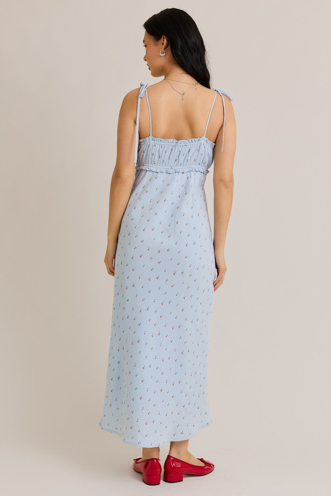 woman wearing a light blue maxi dress with floral print and adjustable tie straps, shown from the back