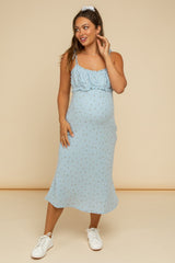 woman wearing a light blue maternity dress with floral print and a ruffled neckline, showing her baby bump