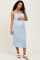 woman wearing a light blue maternity dress with floral print and adjustable straps, holding her baby bump