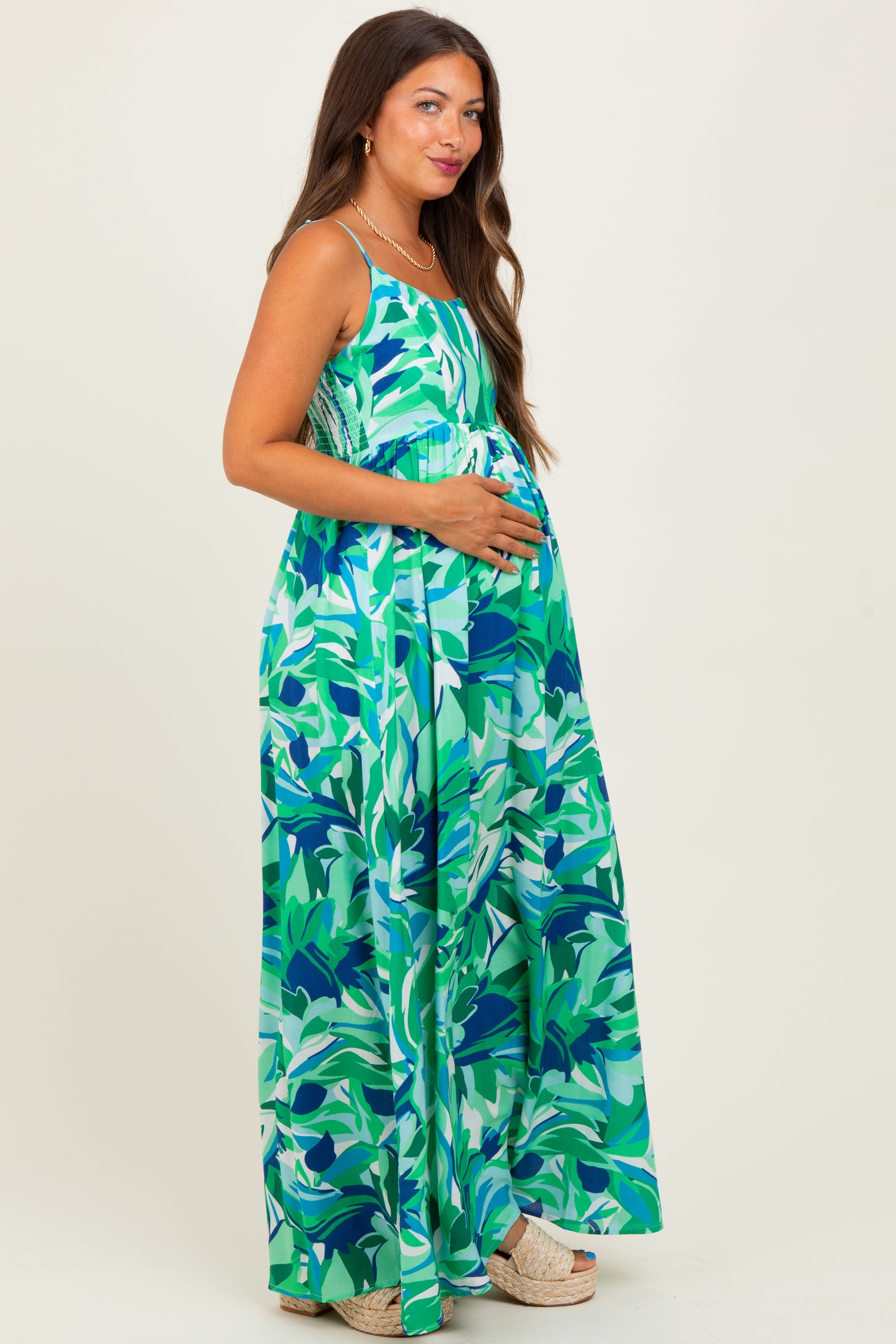 woman wearing a floral print maternity maxi dress in shades of green, holding her baby bump