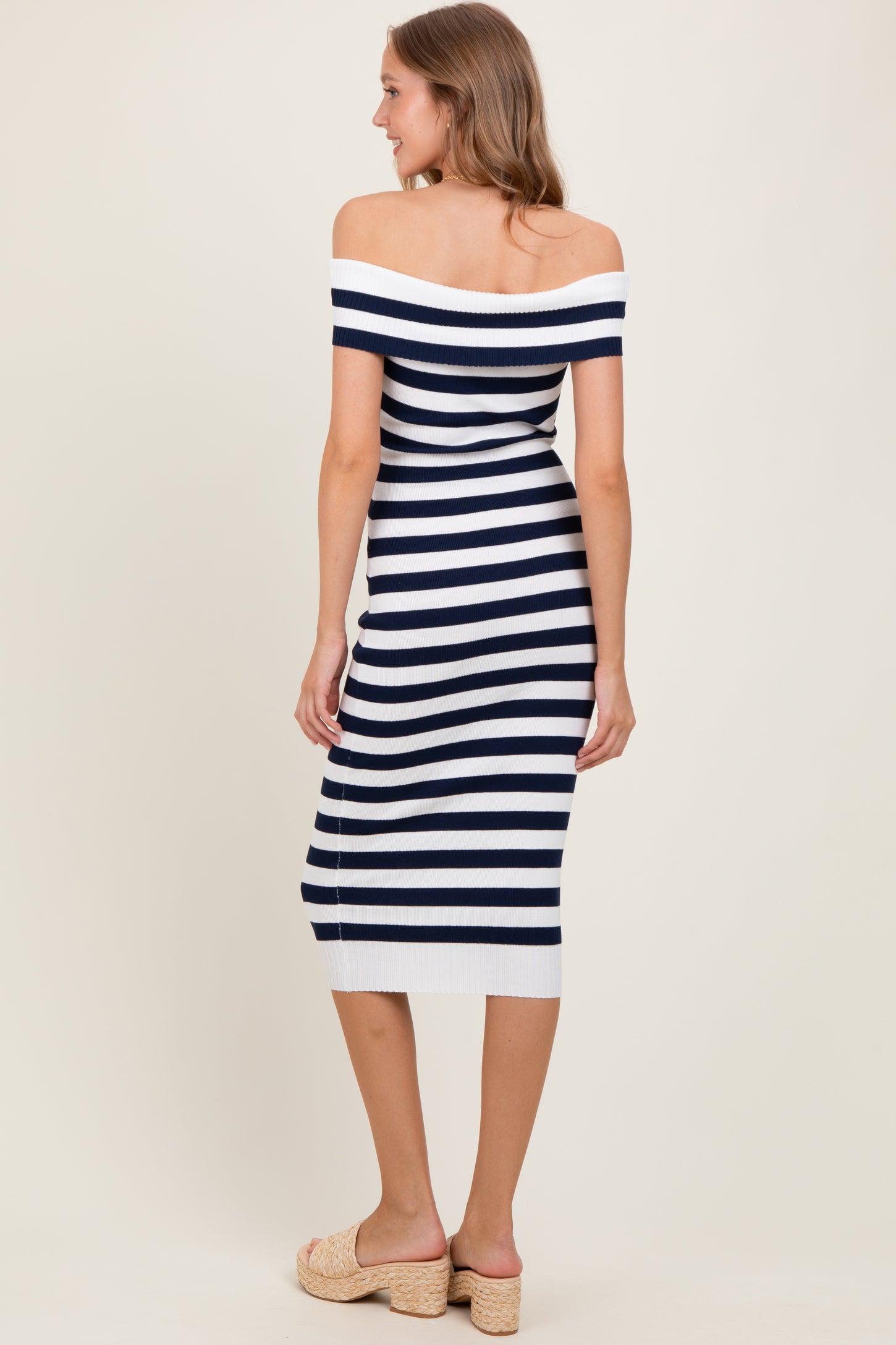 woman wearing a navy and white striped off-the-shoulder midi dress, standing with her back to the camera, and wearing beige wedges