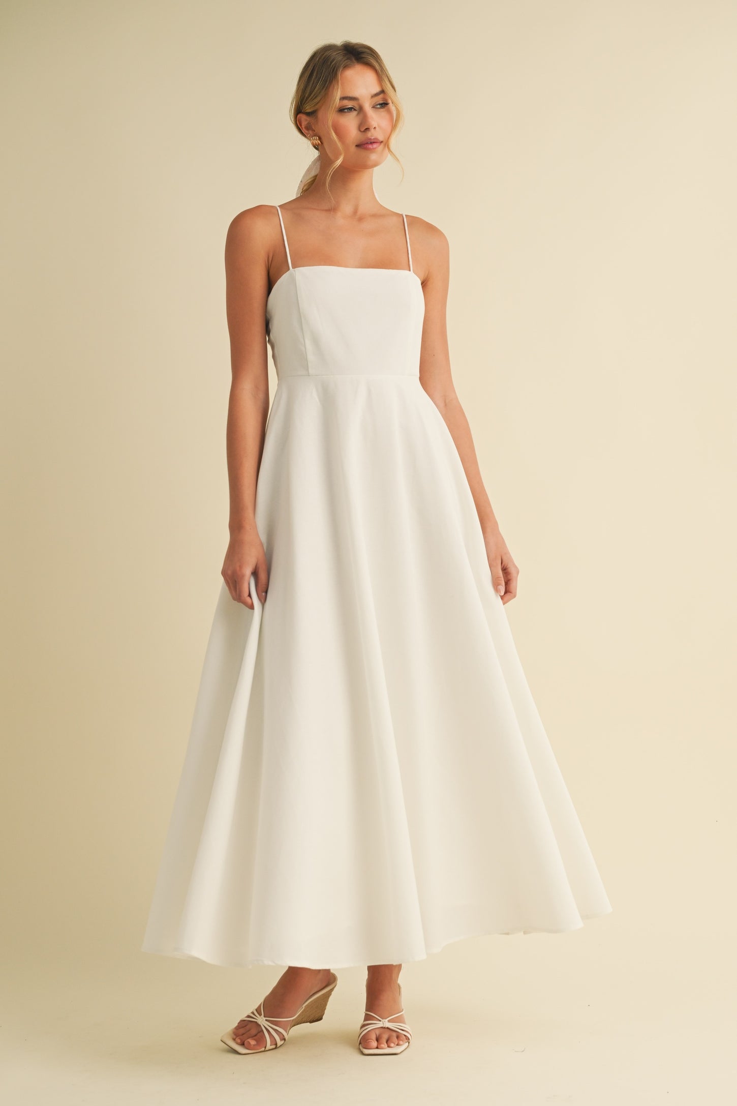 woman wearing a white spaghetti strap maxi dress with a fitted bodice and flowing skirt