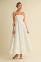 woman wearing a white spaghetti strap maxi dress with a fitted bodice and flowing skirt