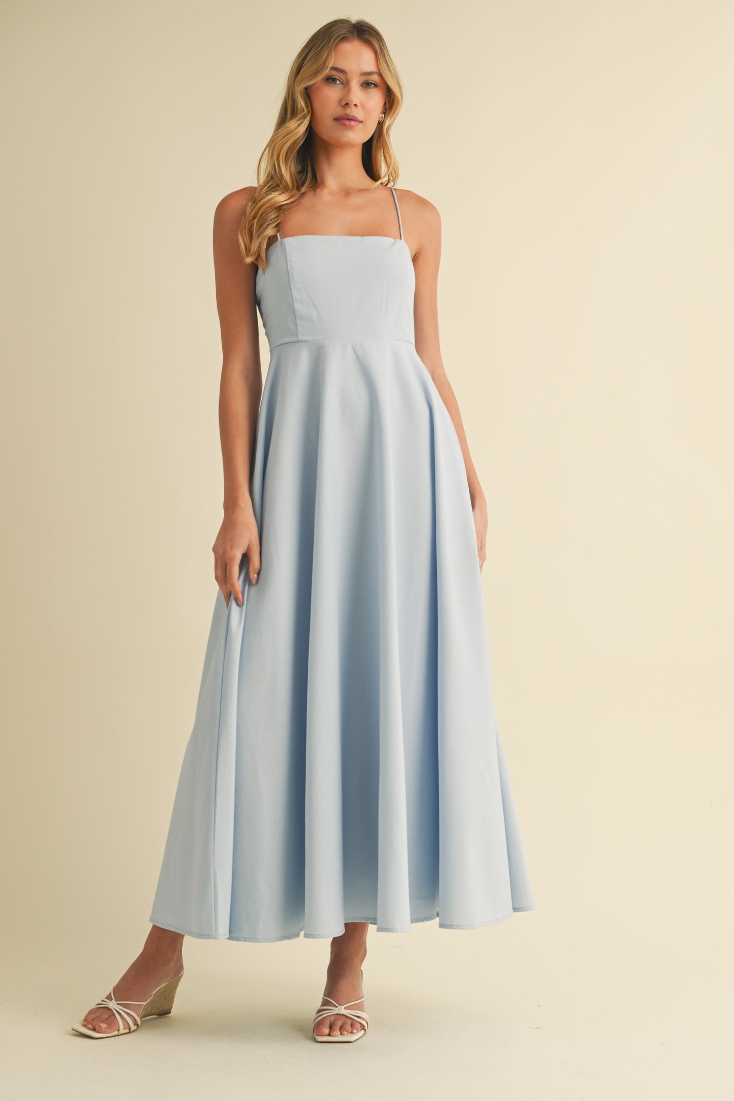 woman wearing a light blue spaghetti strap maxi dress with a fitted bodice and flowy skirt