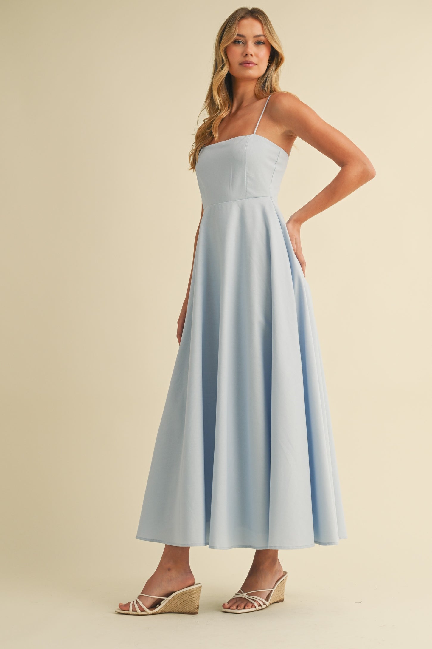 woman wearing a light blue spaghetti strap maxi dress with a fitted bodice and flared skirt