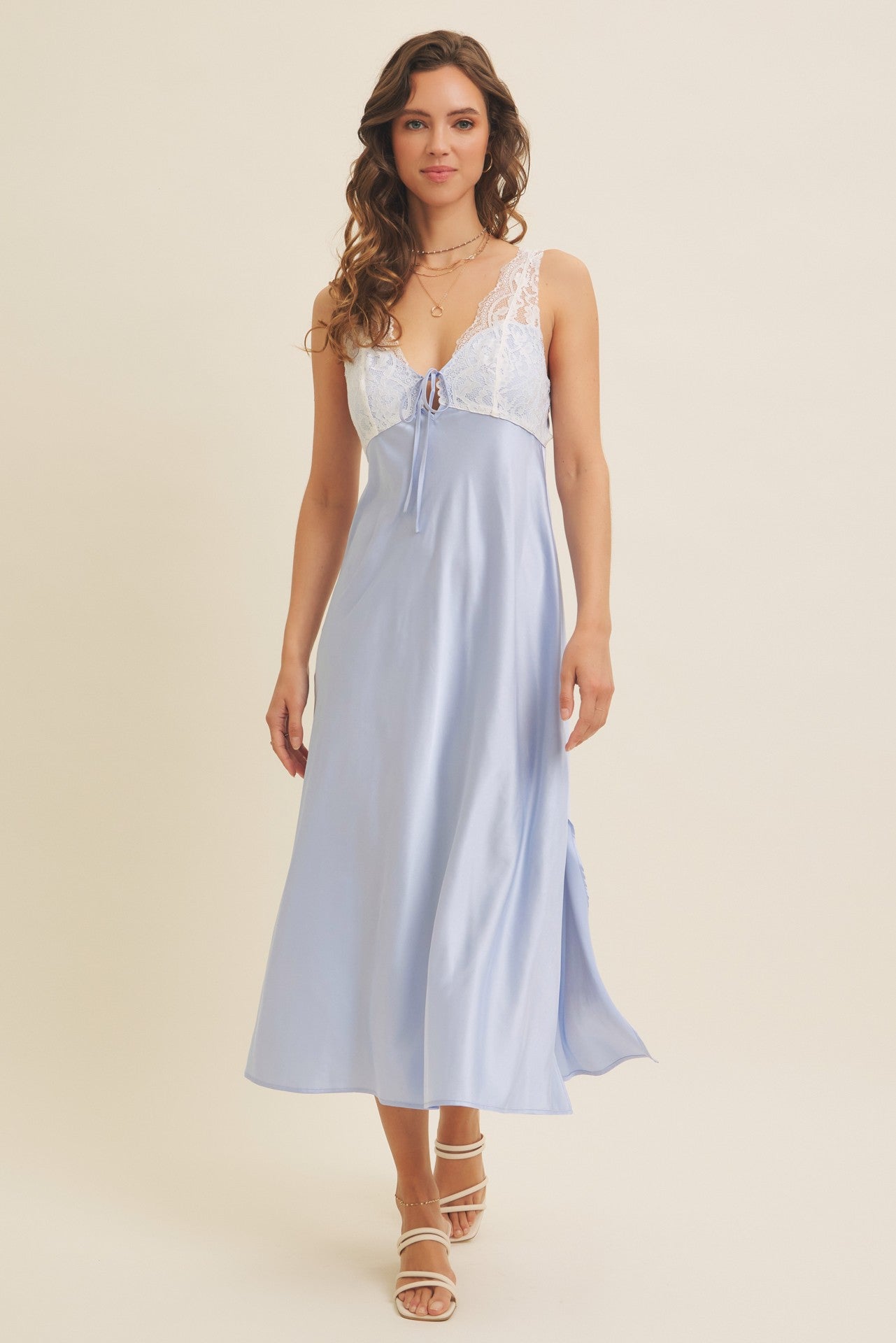 woman wearing a light blue satin slip dress with lace trim and adjustable tie detail, styled with strappy sandals