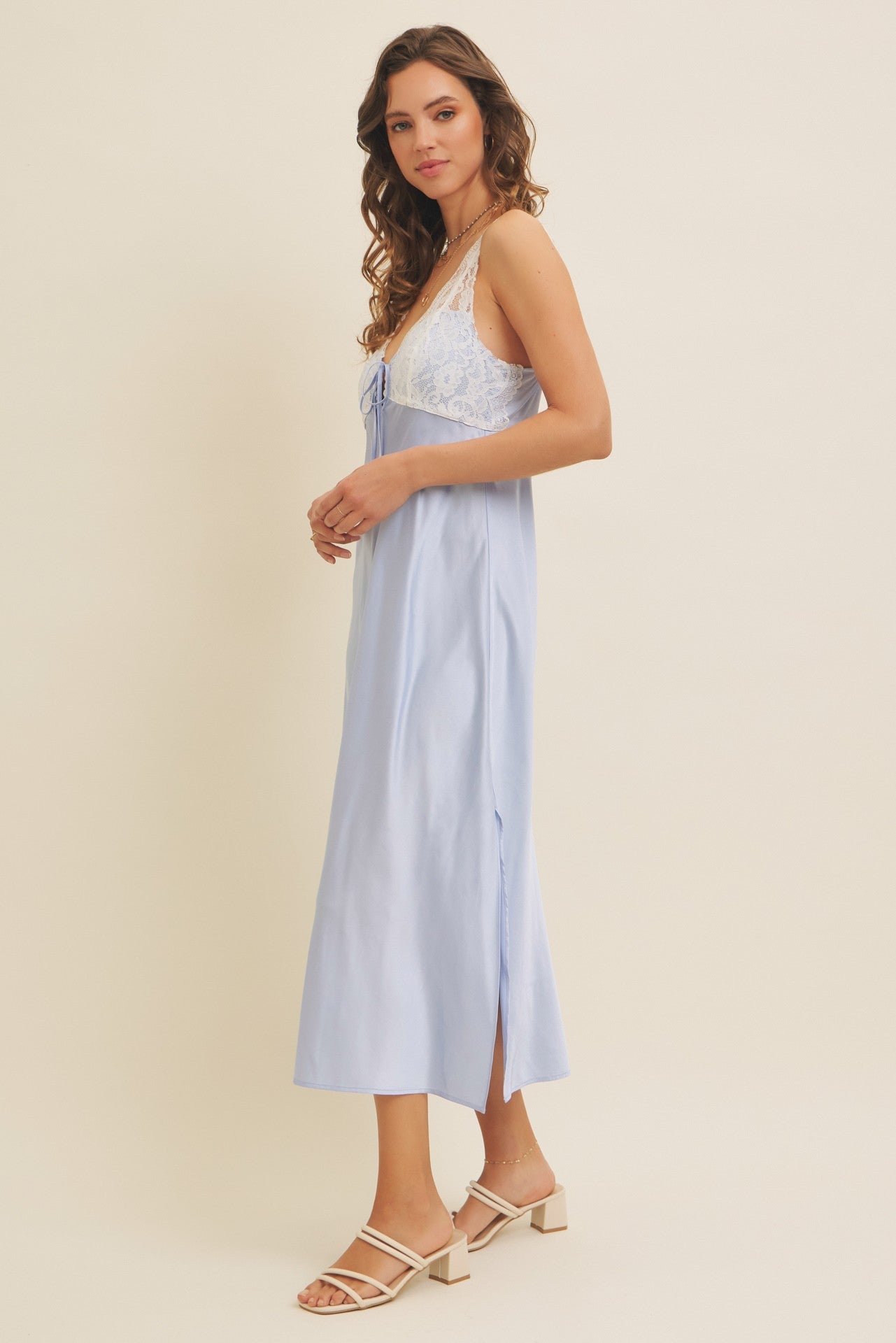 woman wearing a light blue sleeveless midi dress with lace details and a side slit