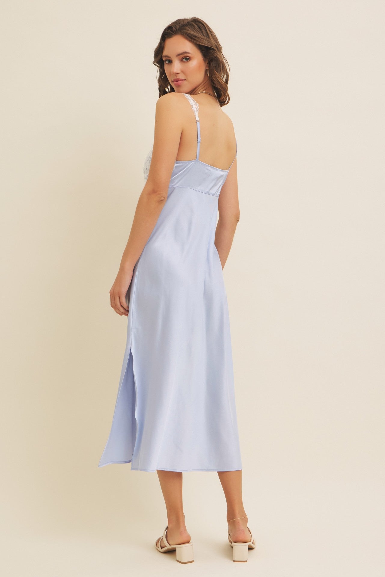 woman wearing a light blue sleeveless midi dress with a slit and lace detailing on the back