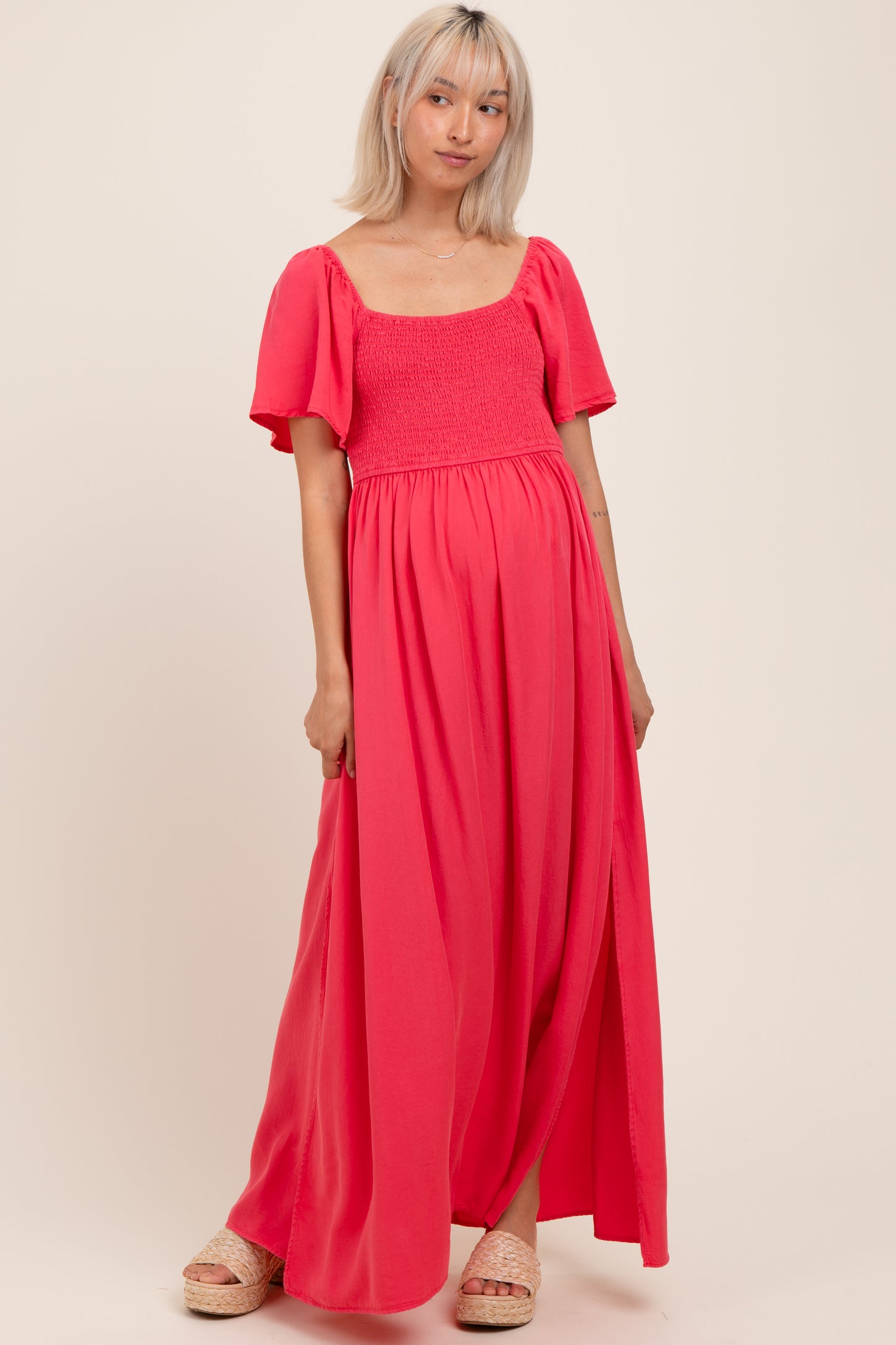 woman wearing a bright pink maternity maxi dress with a square neckline and short puff sleeves, showing her baby bump
