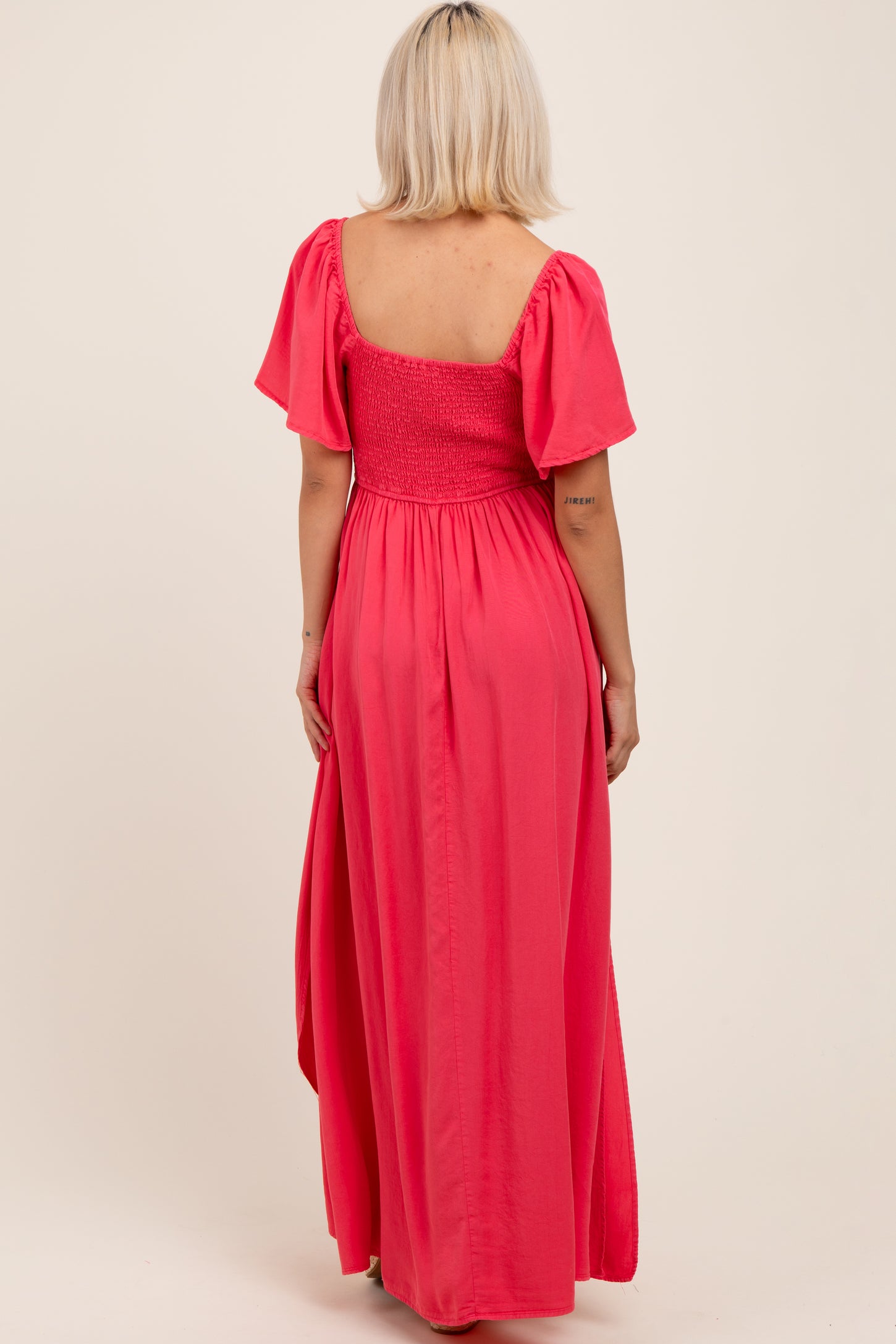 woman wearing a pink maternity maxi dress with short puff sleeves and a smocked bodice, showing her back