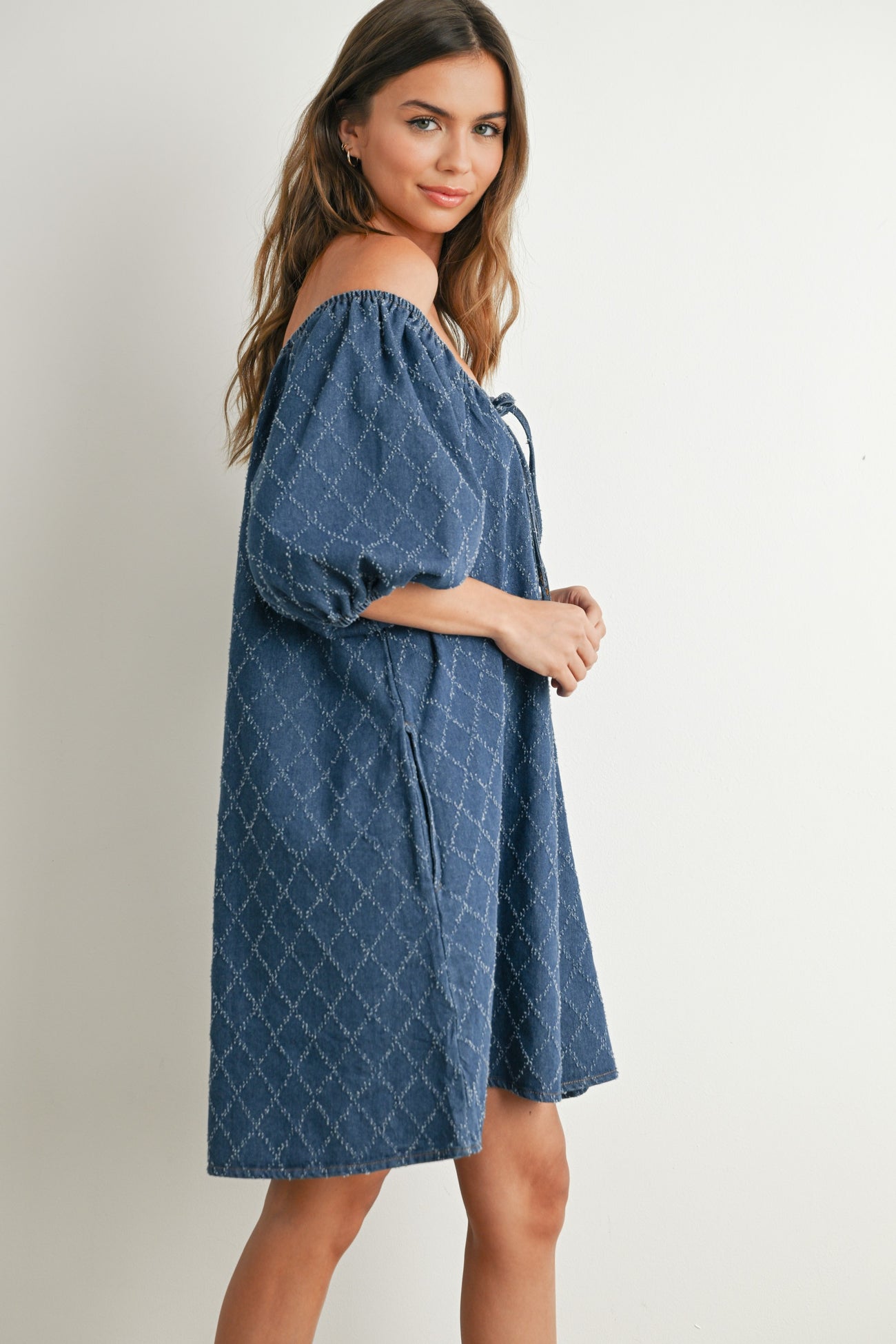 woman wearing a navy off-the-shoulder dress with puff sleeves and a diamond pattern design