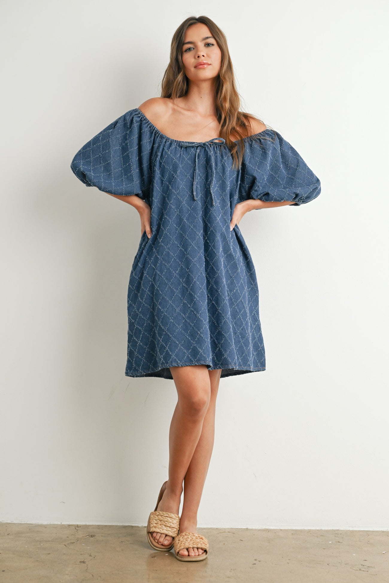 woman wearing a navy off-the-shoulder denim dress with puff sleeves and a relaxed fit, posing against a white background