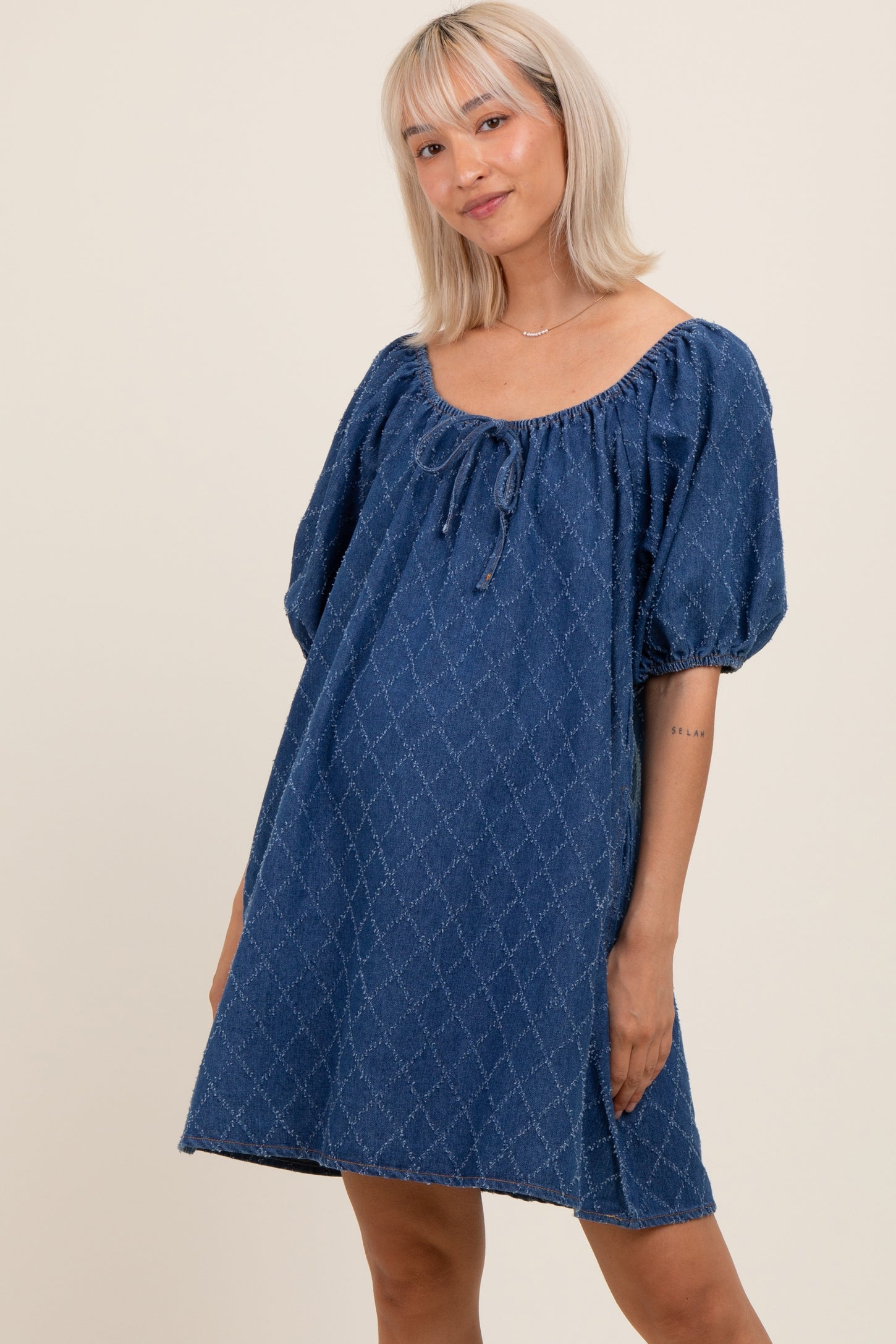 woman wearing a denim puff sleeve maternity dress with a tie detail at the neckline and a relaxed fit