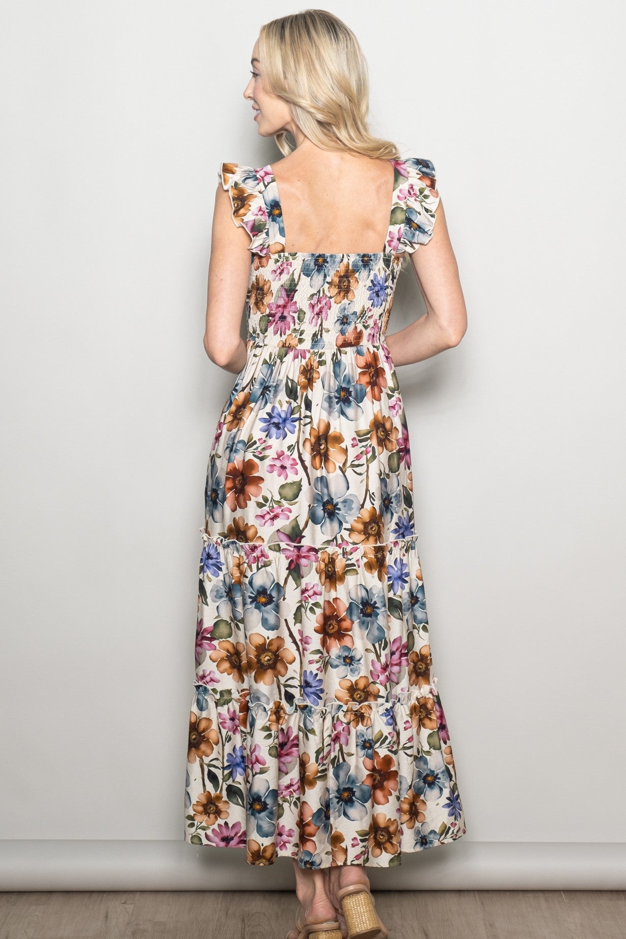 woman wearing a floral maxi dress with ruffle sleeves and a smocked back, standing with her back to the camera