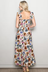 woman wearing a floral maxi dress with ruffle sleeves and a smocked back, standing with her back to the camera