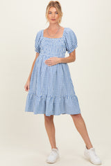 woman wearing a blue and white gingham maternity dress with puff sleeves and a ruffled hem, holding her baby bump